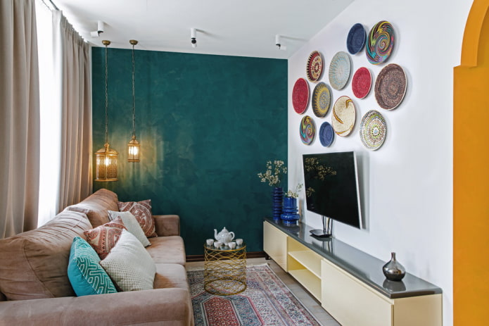 Televizorius ant sienos su dekoratyviniu skydeliu salėje